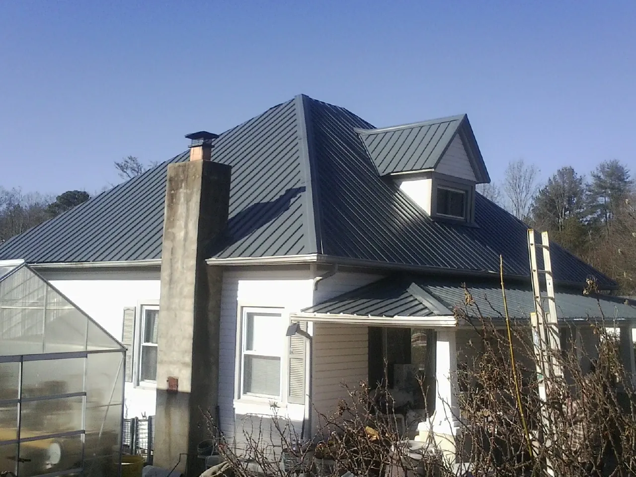 Dark blue standing seam metal roof on a white farmhouse with dormer — Slate & Tile Roof Repair by Roofing Brothers in Friend