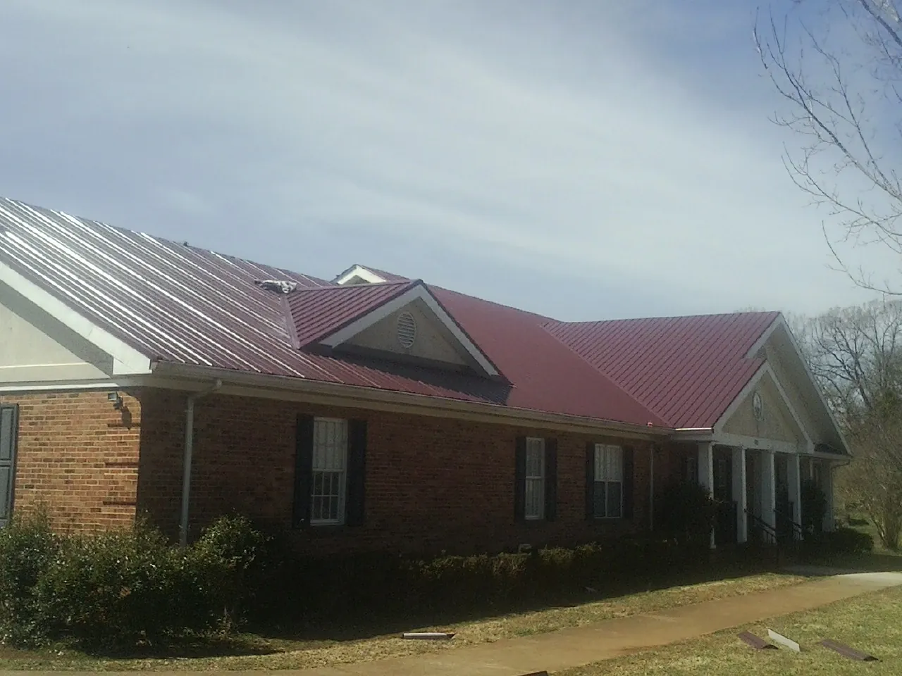 Red metal roof with gabled entries on a long brick building, from a Hail Damage Roof Repair job in Friend