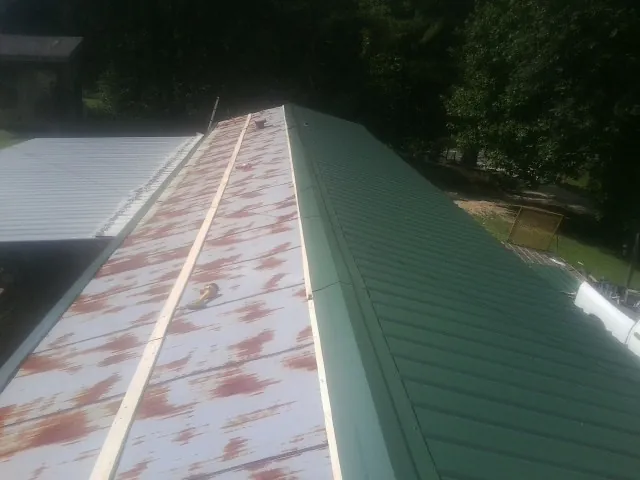 Old rusted panels beside newly installed green metal roofing — Wind Damage Roof Repair by Roofing Brothers in Friend