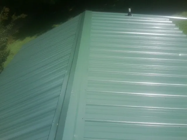 New green metal panels meeting at the ridge of a roof — Flat Roof Repair work by our crew in Friend