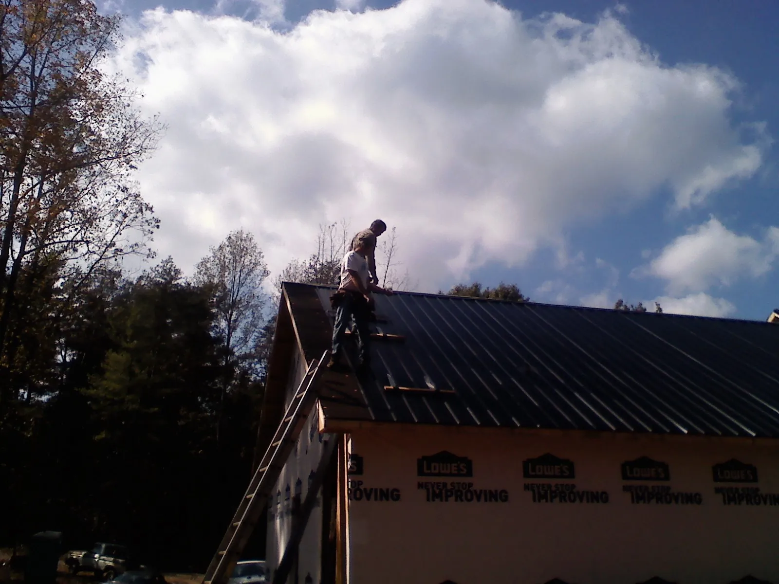 Roofer fastening dark metal panels high against a cloudy sky, from a Roof Inspection job in Friend