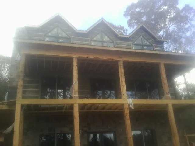 Dormers and porch framing on a large log home under construction — Roof Coating work by our crew in Friend