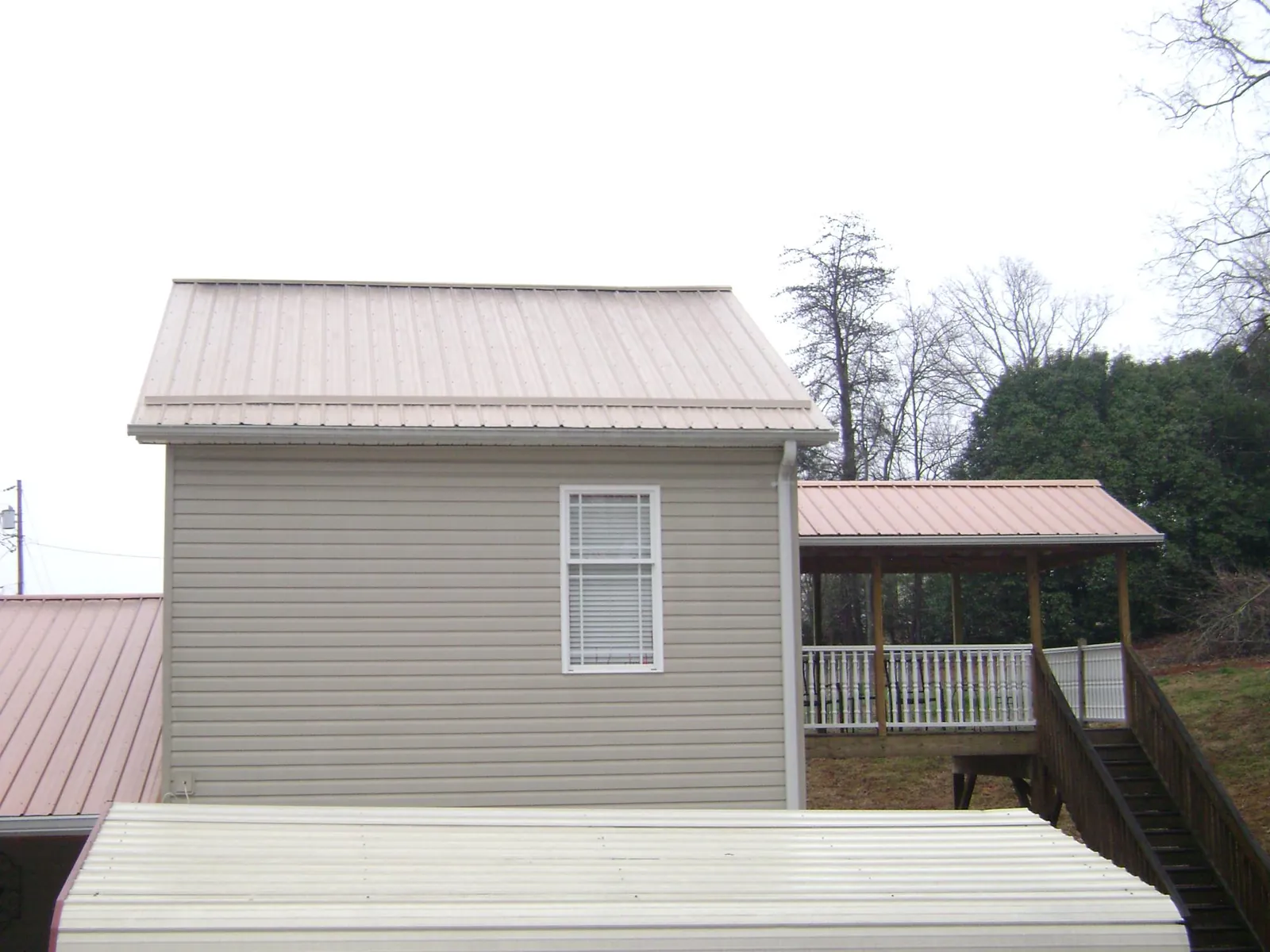 Tan metal roofs on a two story addition and attached porch, from a Roof Replacement job in Friend